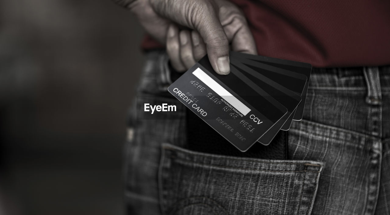 Midsection of person holding credit cards against black background