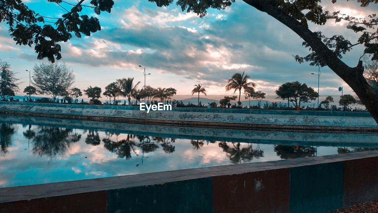 REFLECTION OF TREES IN SWIMMING POOL AGAINST SKY