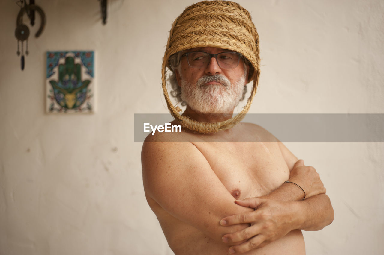 Shirtless senior man wearing wicker basket at home