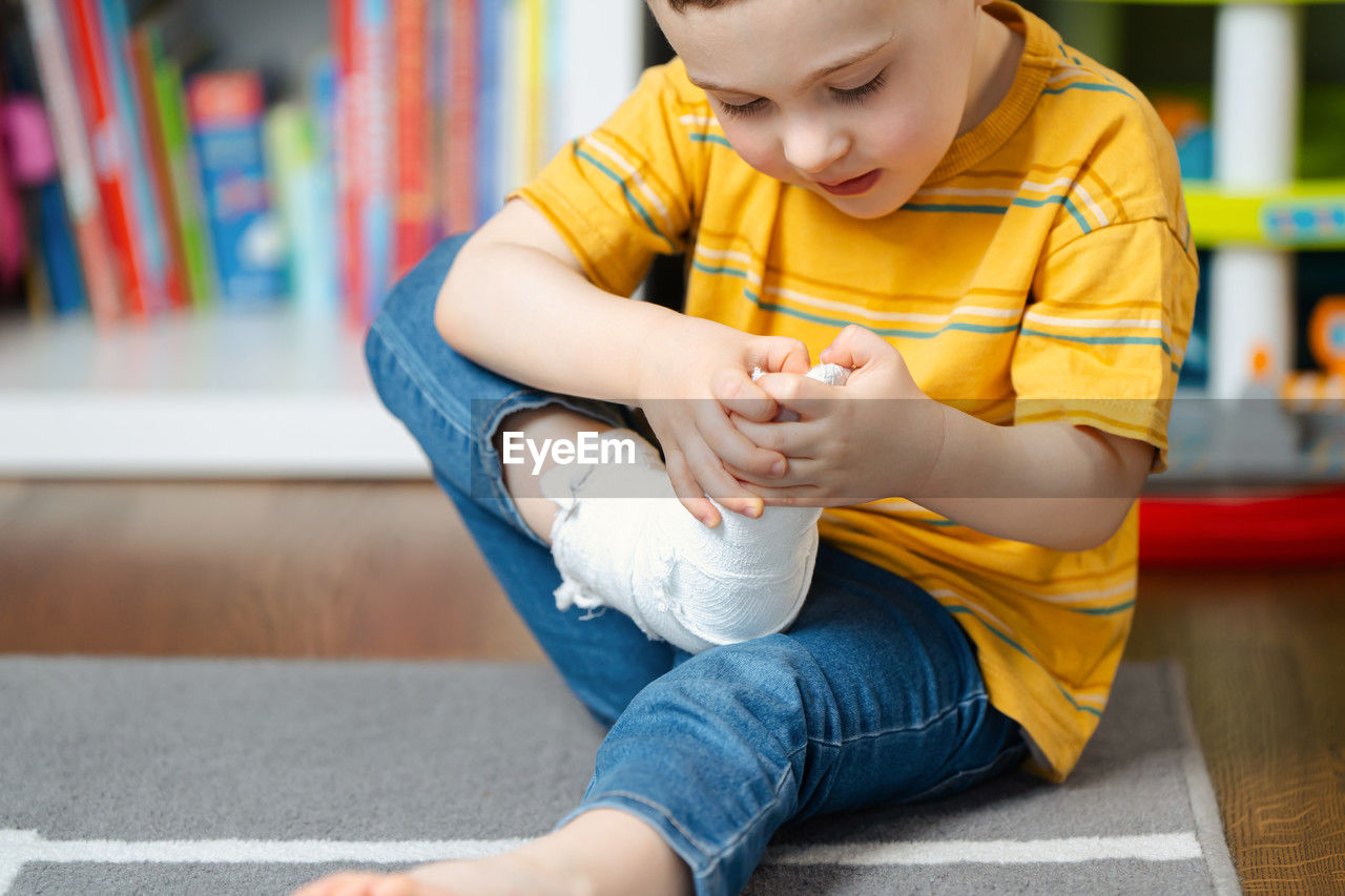 A little toddler boy holds his leg in a cast with his hands. fracture of a foot and finger 