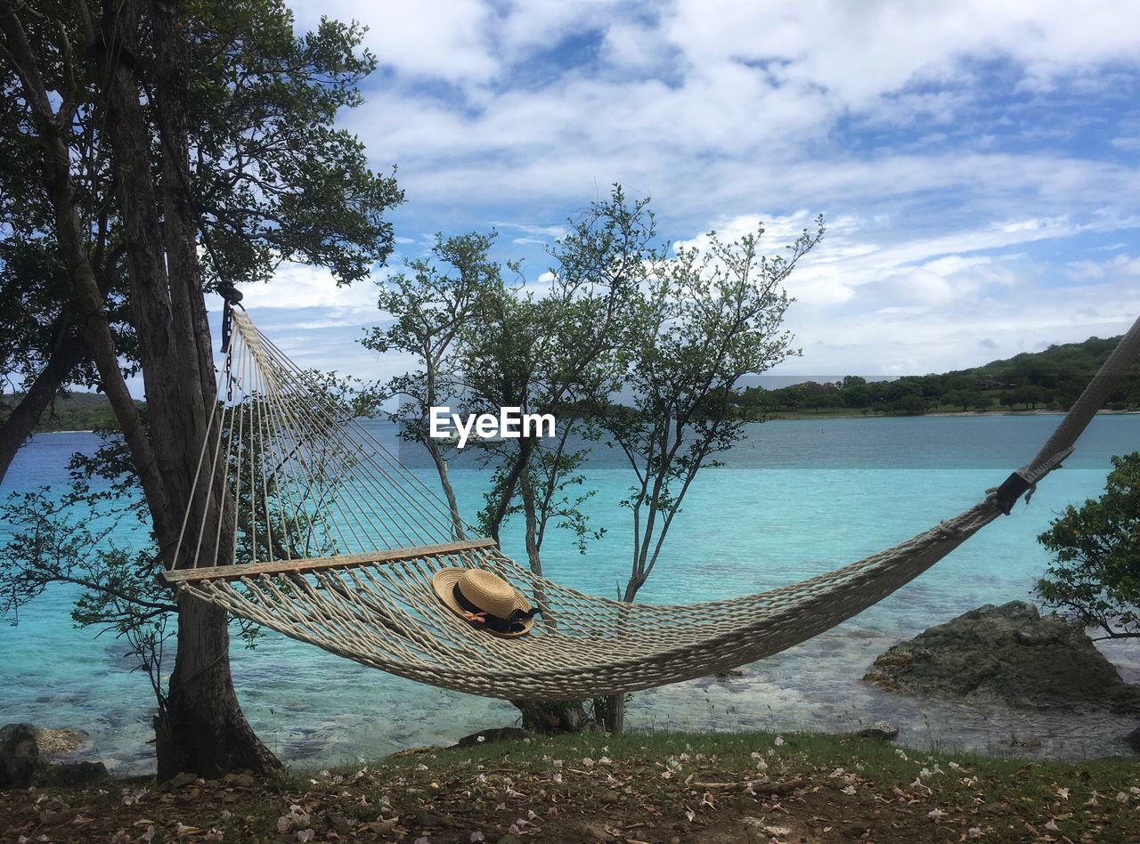 Hammock by lake against cloudy sky