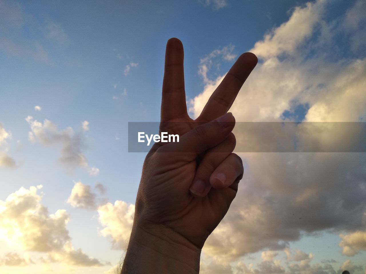 Low angle view of person hand gesturing peace sign against sky