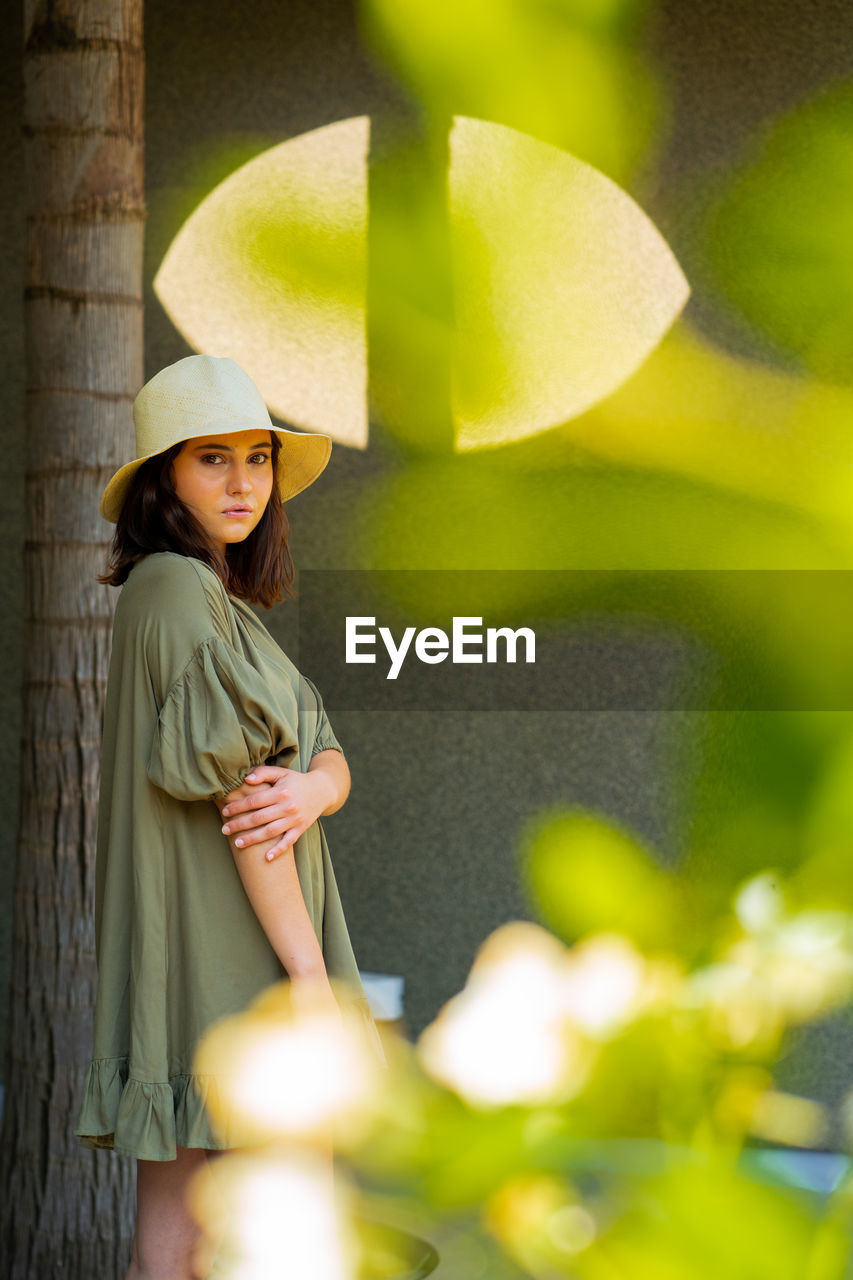 Portrait of a smiling woman standing outdoors, surrounded by plants and trees.