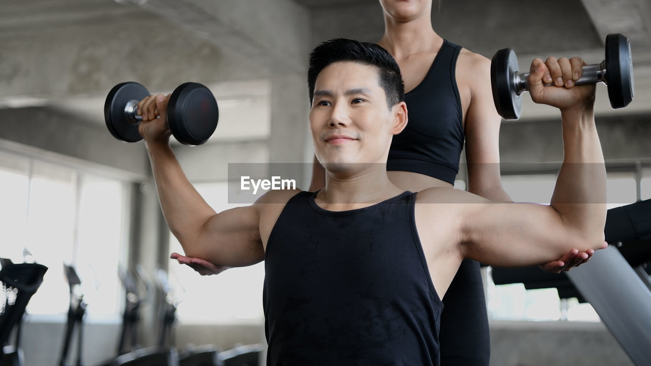 Woman assisting friend in exercising at gym