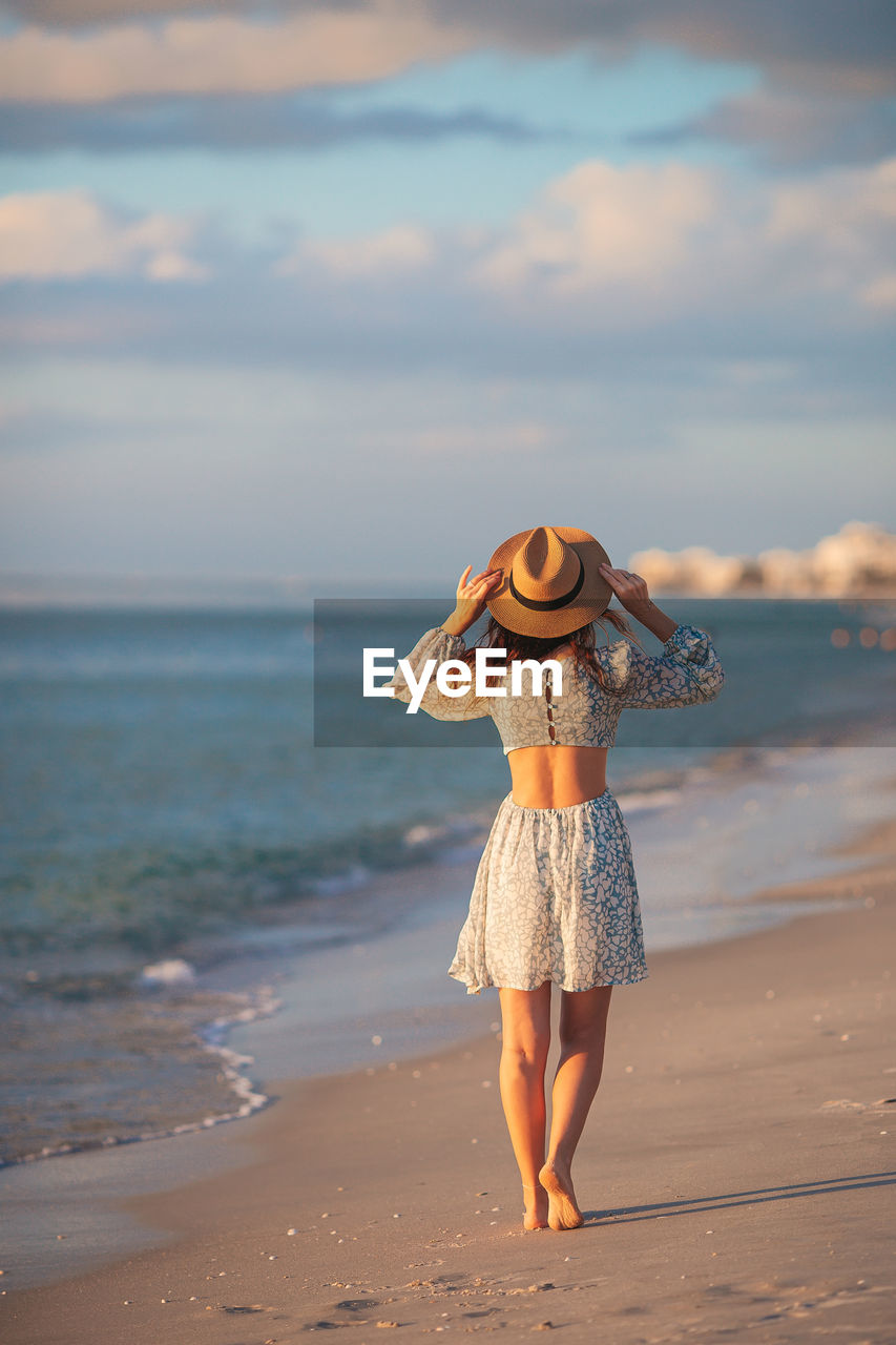 rear view of woman standing at beach against sky