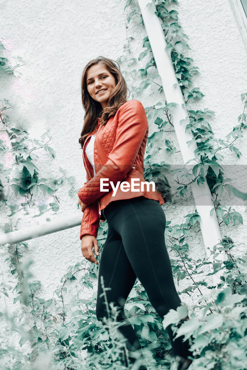 Portrait of smiling young woman standing against wall