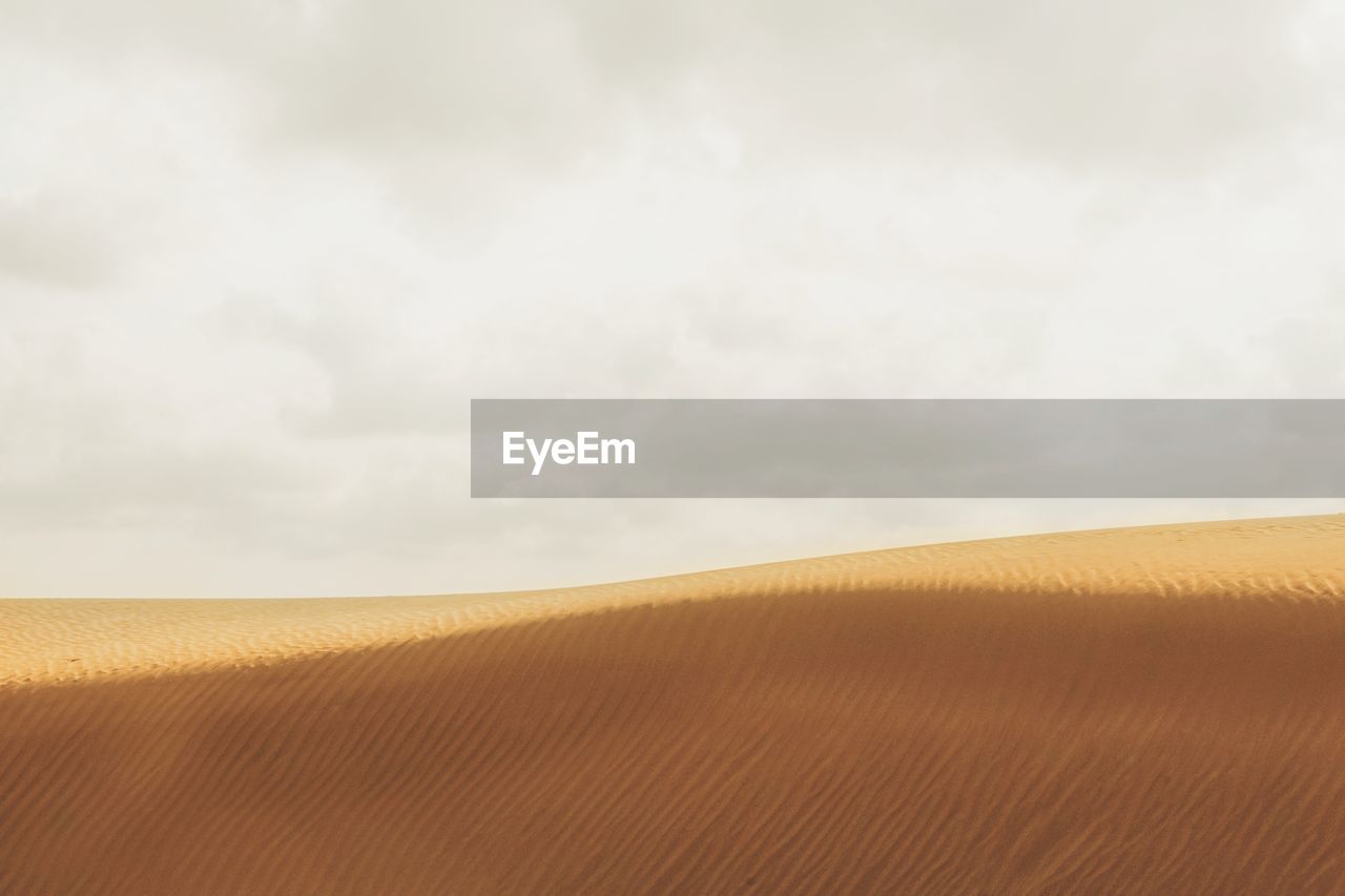 SCENIC VIEW OF SAND DUNE AGAINST SKY