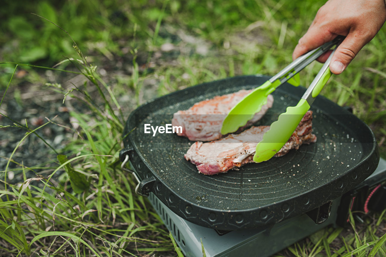 Meat steak fried grill pan on gas stove open air, hand turns over potholders appetizing piece meat