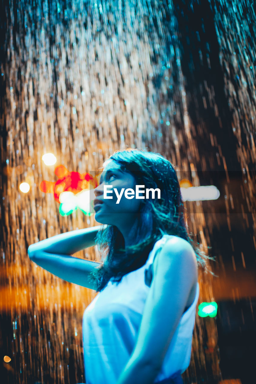 Woman looking away against illuminated waterfall at night