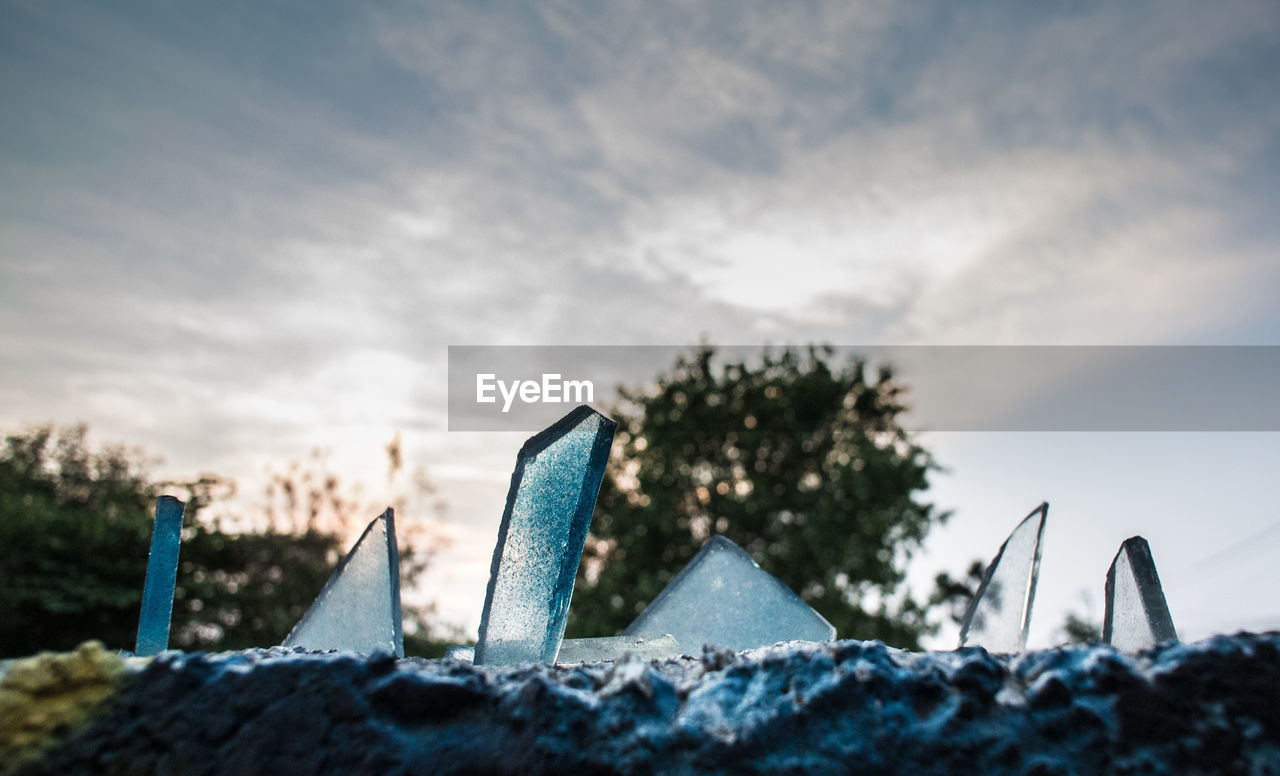 Close-up of broken glasses on retaining wall against cloudy sky