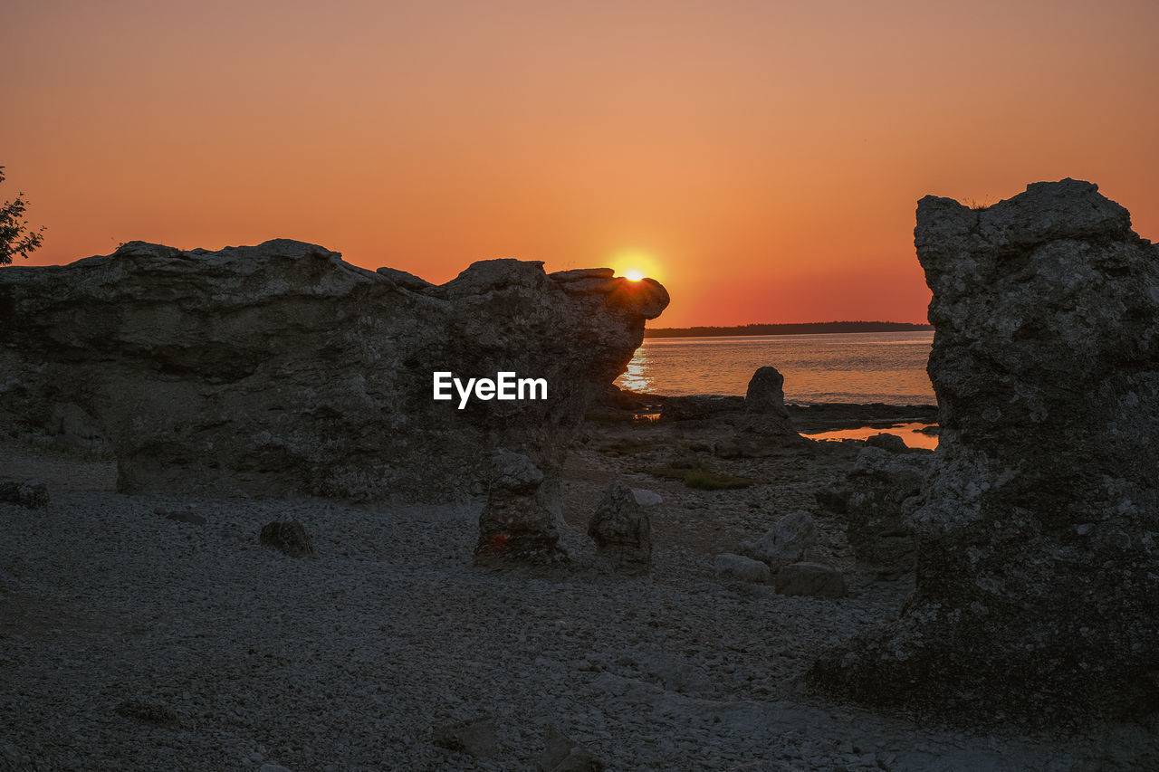 ROCK FORMATIONS ON SHORE AGAINST SKY DURING SUNSET