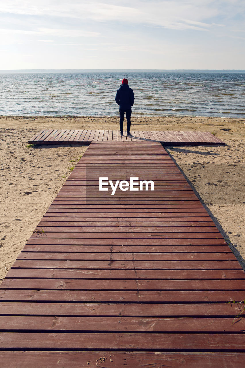  man in a black jacket stands on a wooden platform by the lake