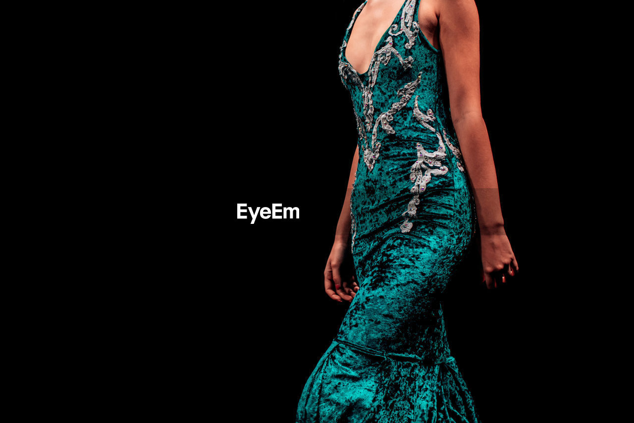 Details of a velvet green evening dress on a female figure on a black background.