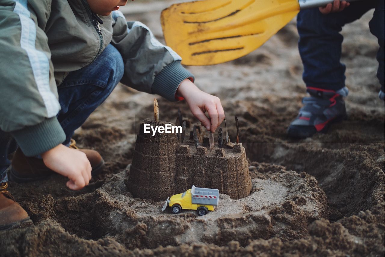 Low section of boy making sand castle by brother at beach