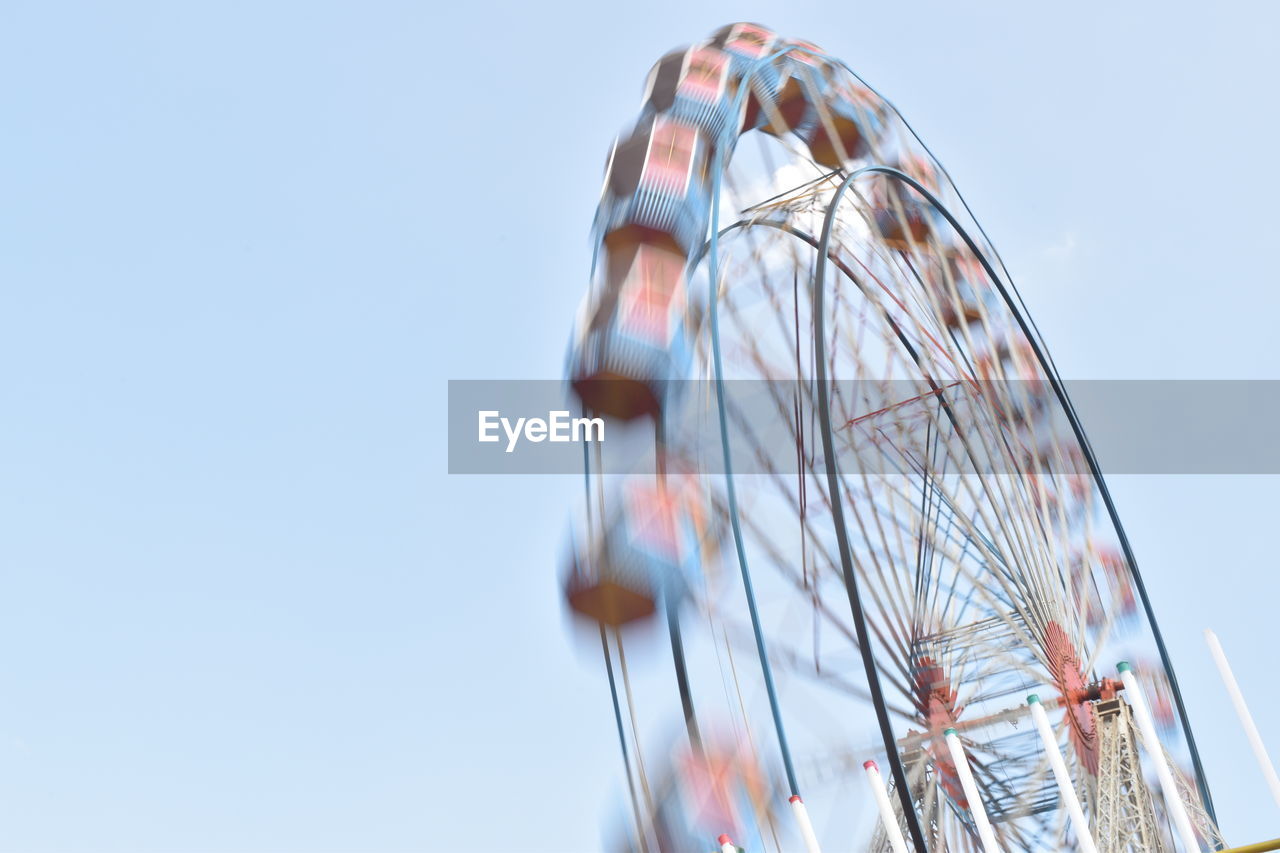 Low angle view of moving ferris wheel against clear sky