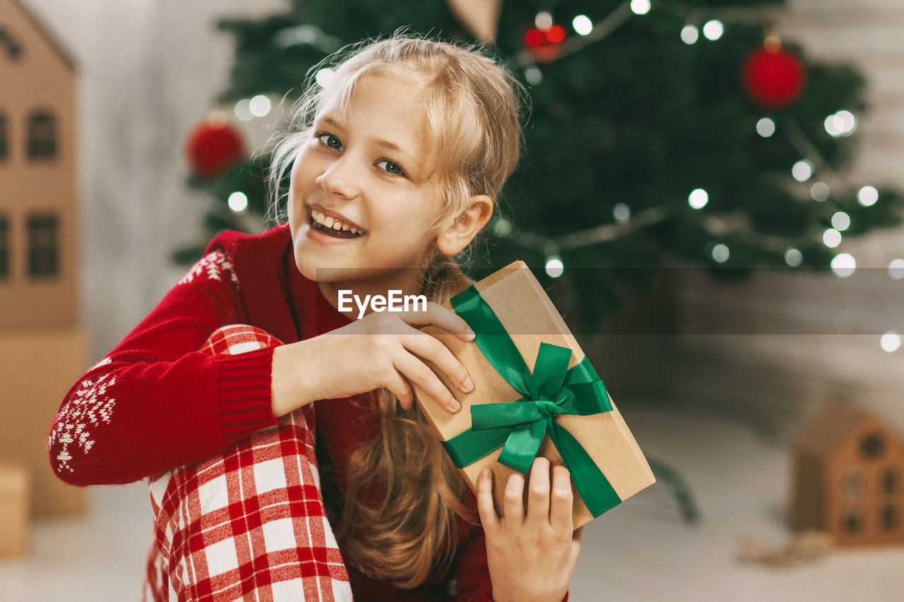 A beautiful little girl looks at the camera and smiles, holding a kraft paper gift 