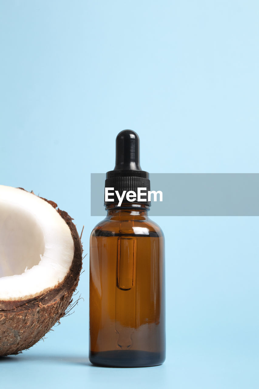 Bottle of coconut oil and fresh coconuts on blue background. coconut natural cosmetics.