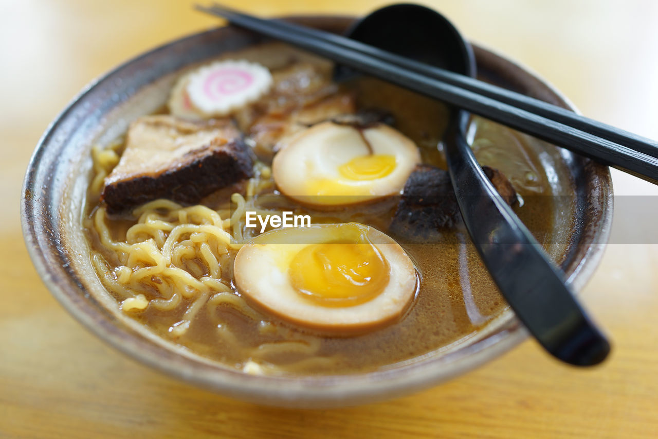 Close-up of ramen noodles in bowl with spoon and chopsticks on wooden table