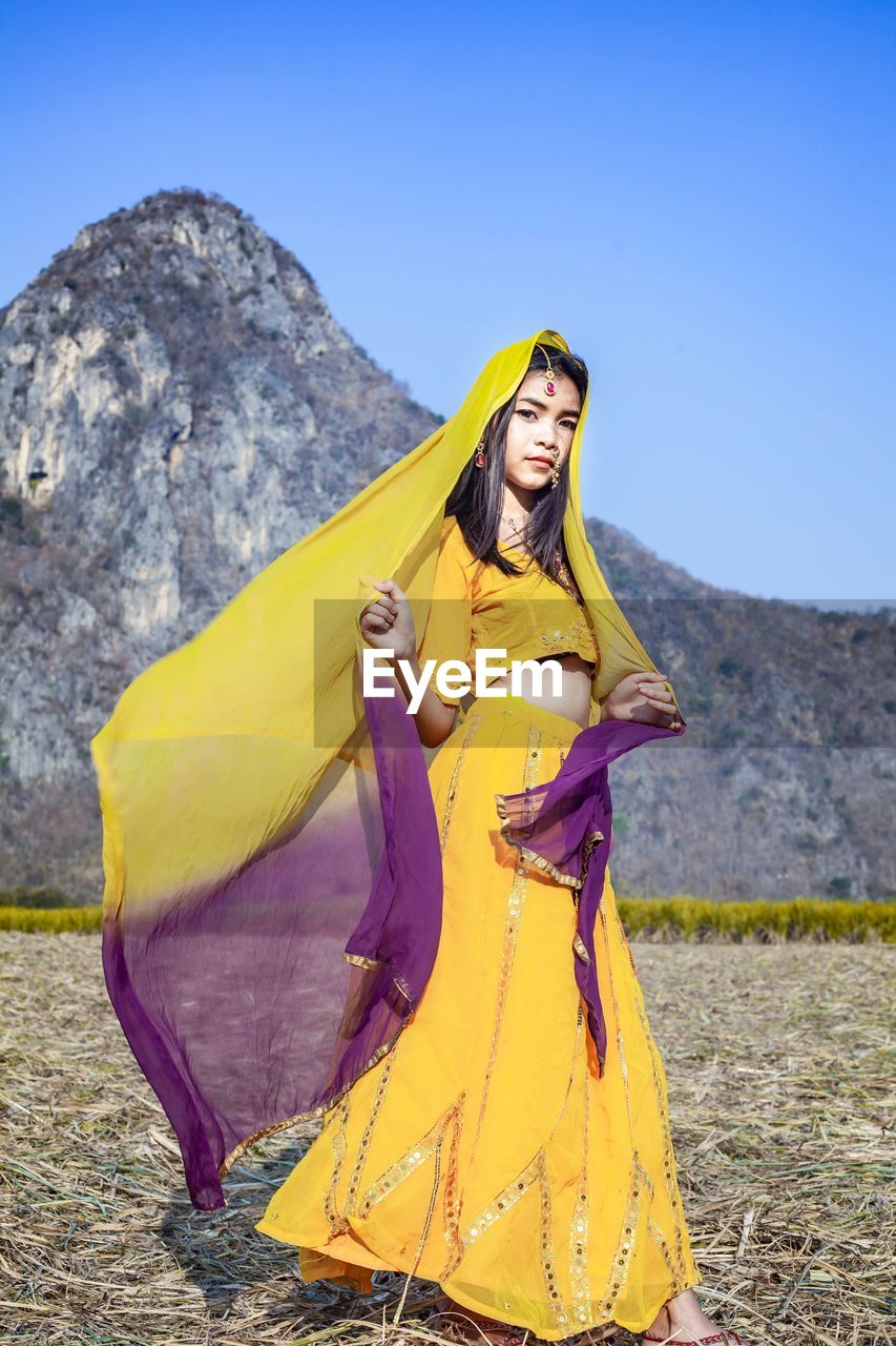 Portrait of woman standing with yellow arabian dress against mountain