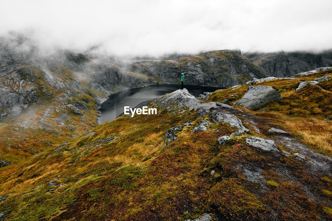 Hiking man at cliff edge with scenic view of lake and mountains at munkebu in lofoten norway