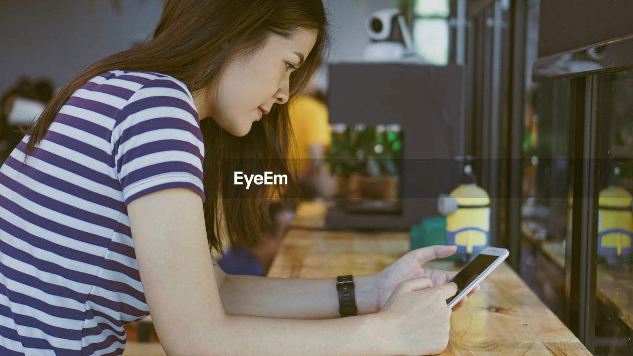 Young woman using smart phone sitting at table in cafe