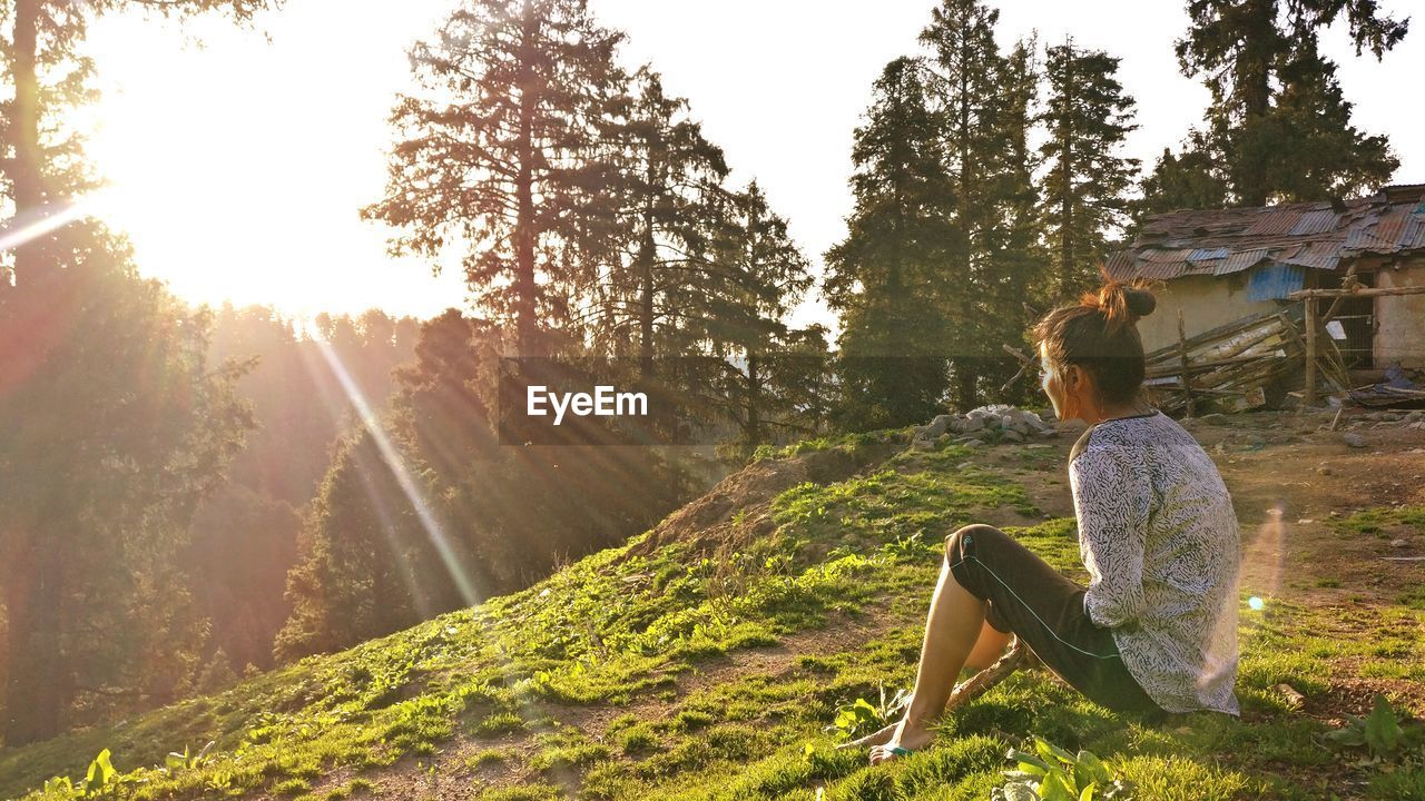 SIDE VIEW OF YOUNG WOMAN SITTING ON LANDSCAPE