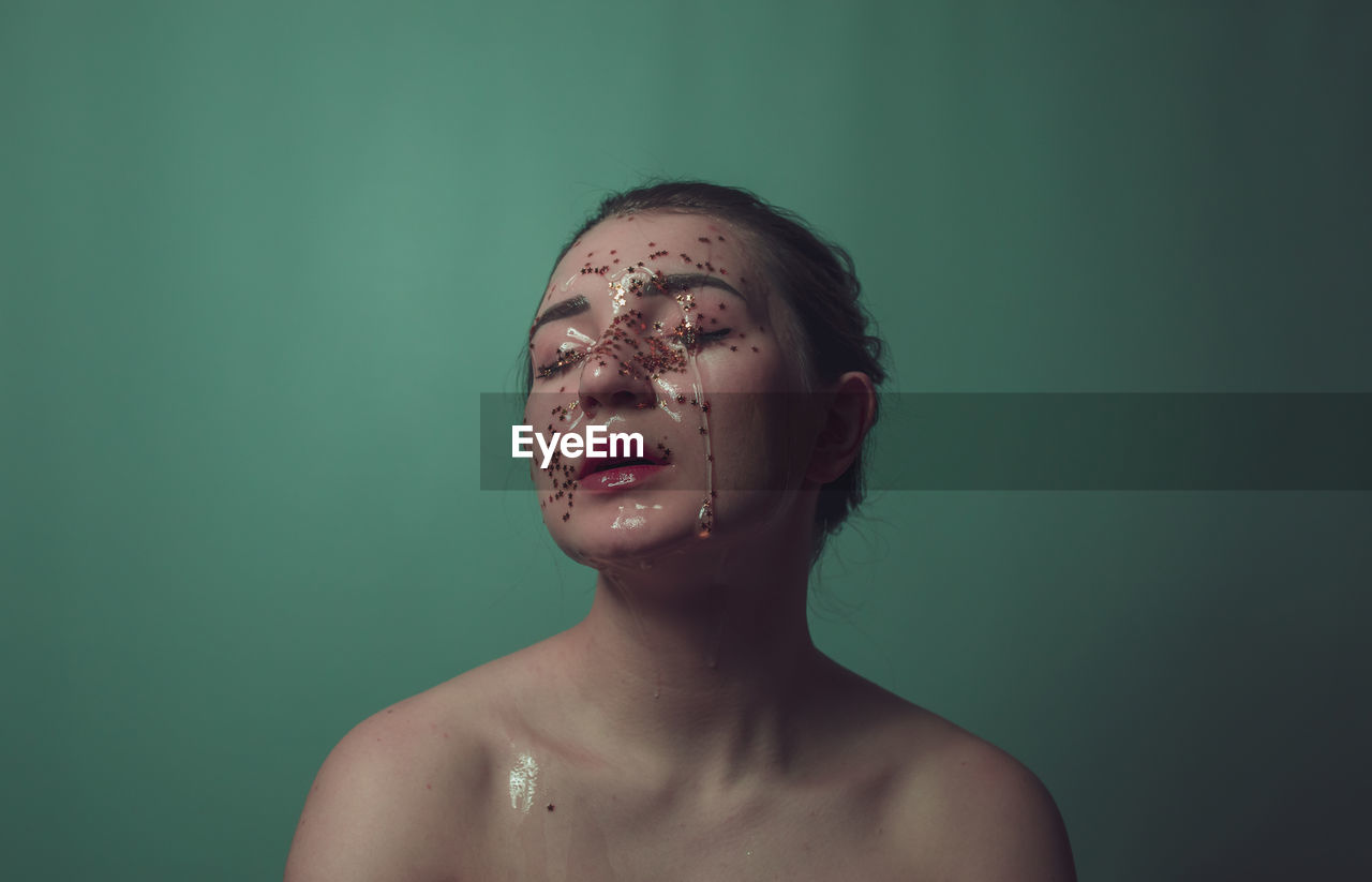 Close-up of shirtless woman with beauty product on face against green background