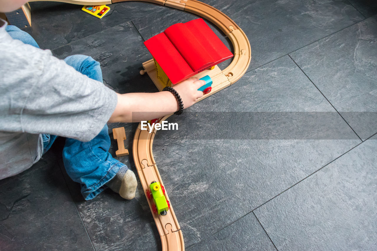 Cropped image of boy playing with train set on floor at home