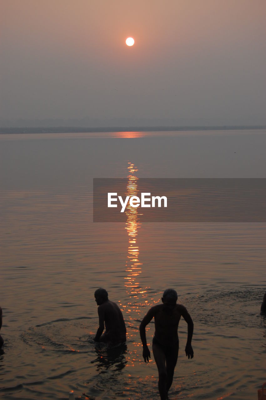 Silhouette people on beach against sky during sunset