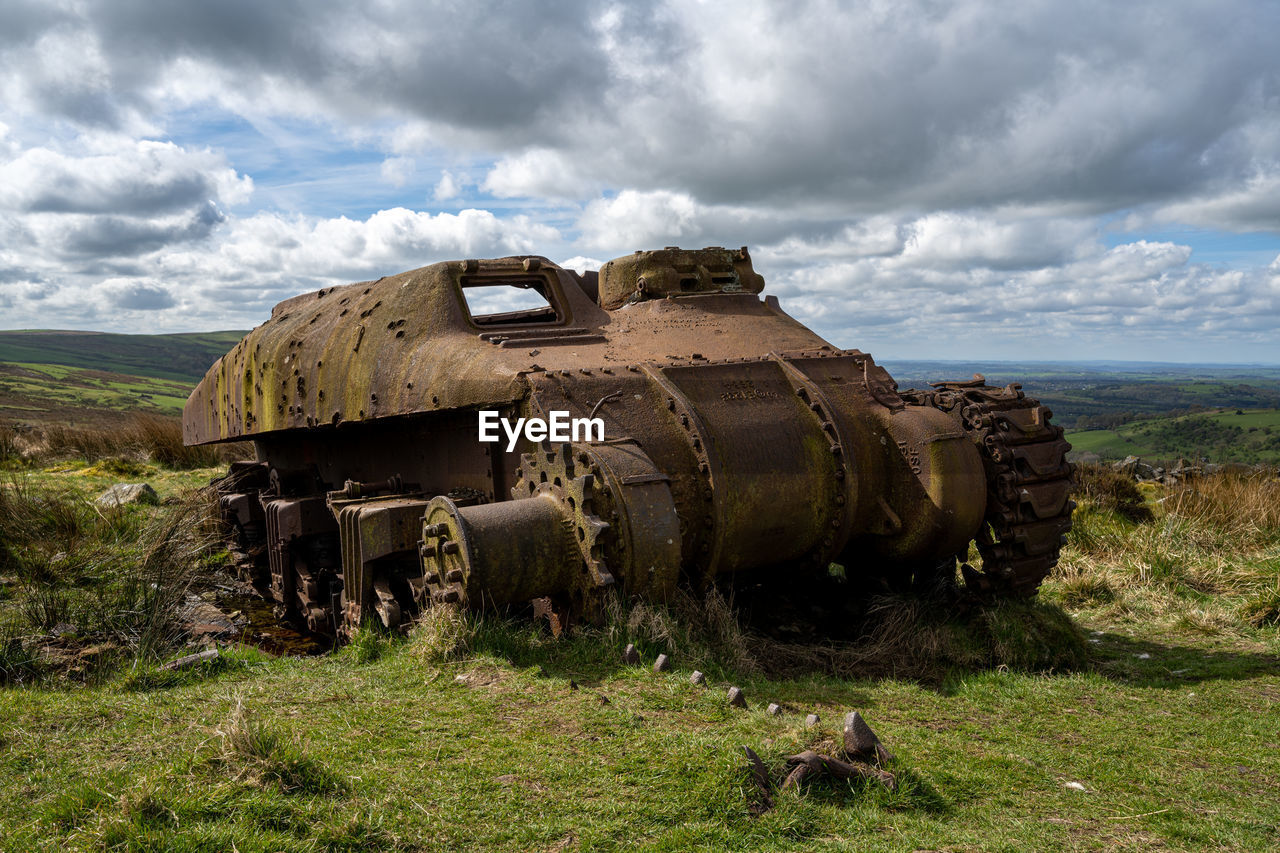 abandoned car on field against cloudy sky