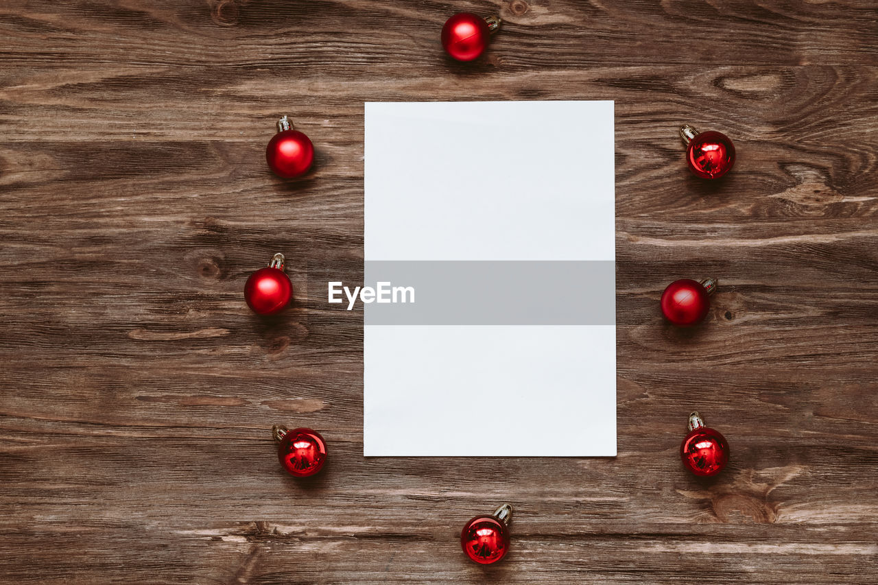 A blank sheet of paper and and red christmas balls on a wooden background. top view, flat lay