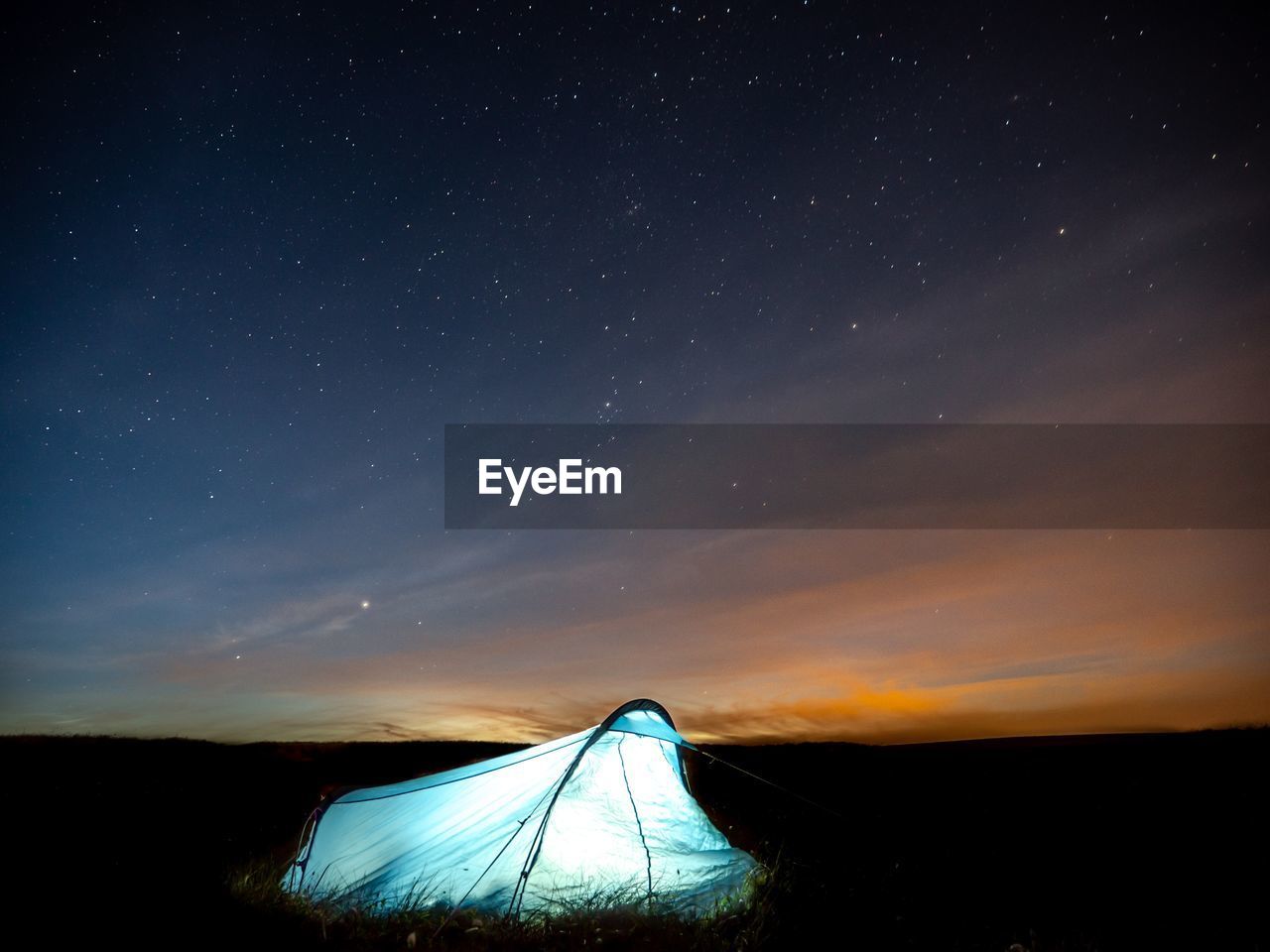 Illuminated tent on field against sky at night