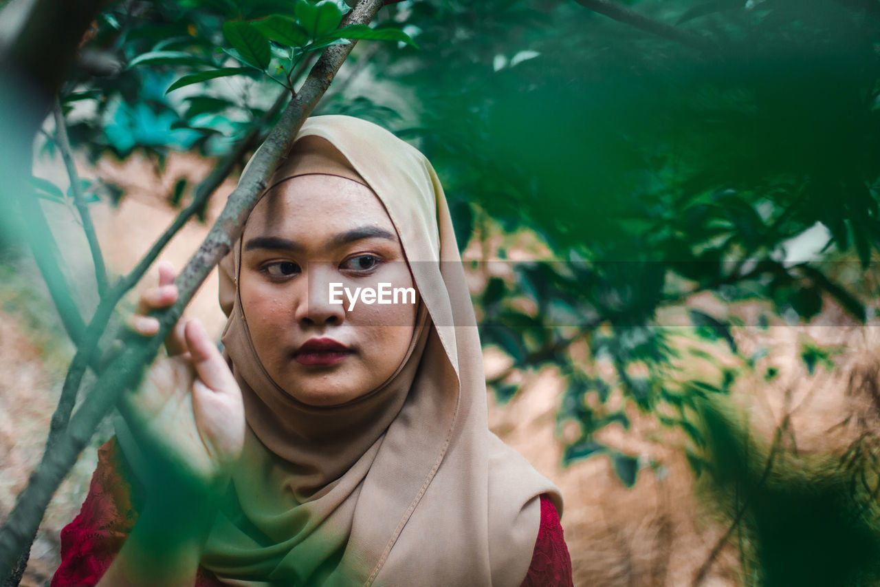 Young woman looking away by trees