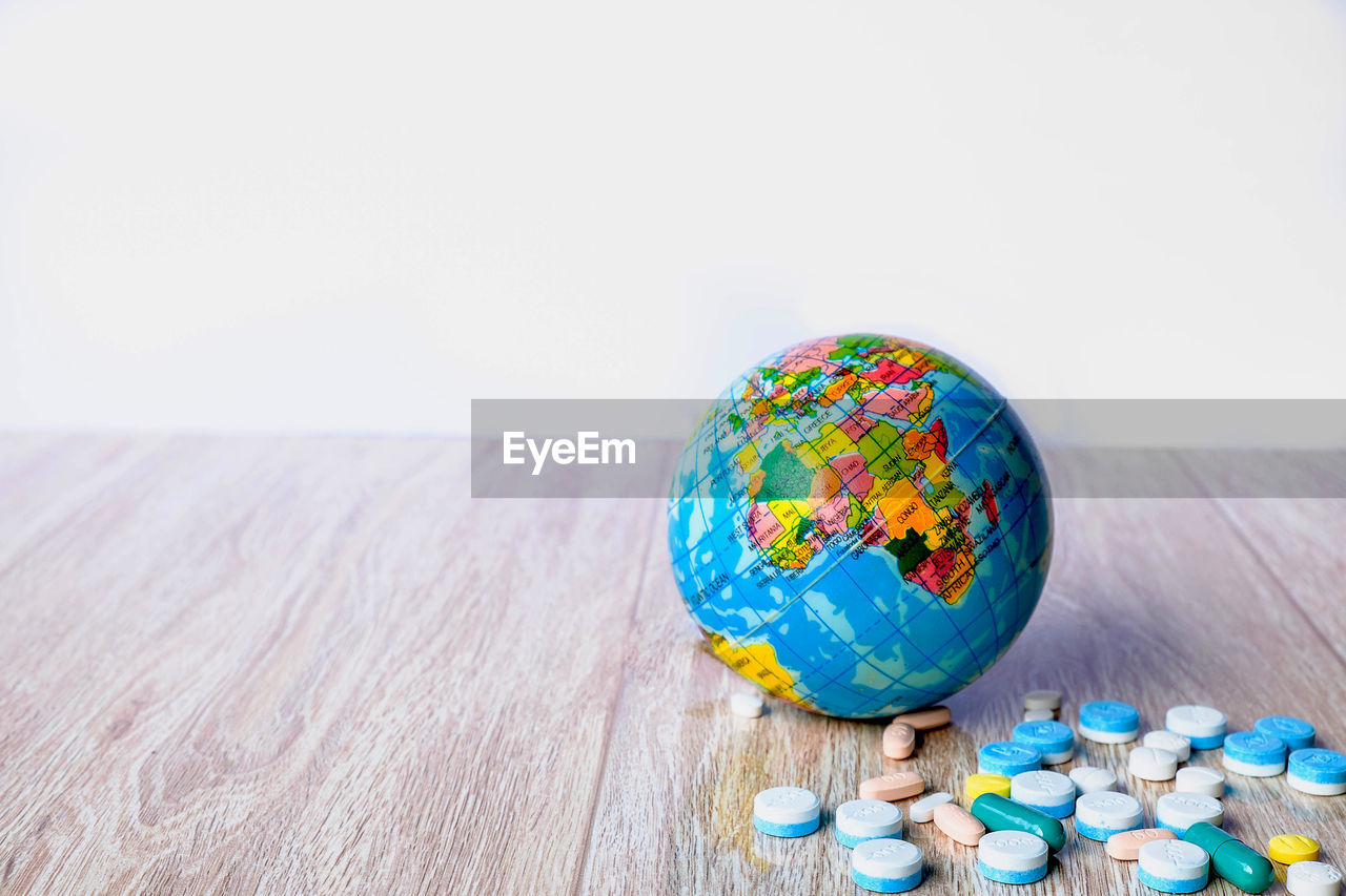 Close-up of globe and medicines on wooden table against white background