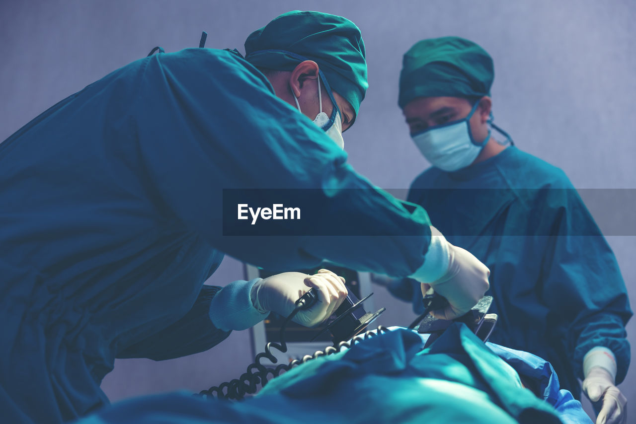 While performing medical surgery inside the operating room, a doctor and nurse use a defibrillator.