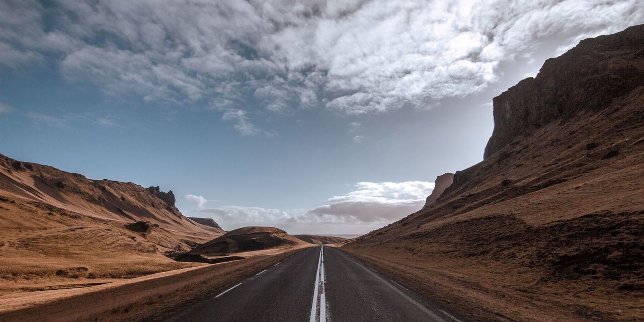 Empty road by mountains against sky