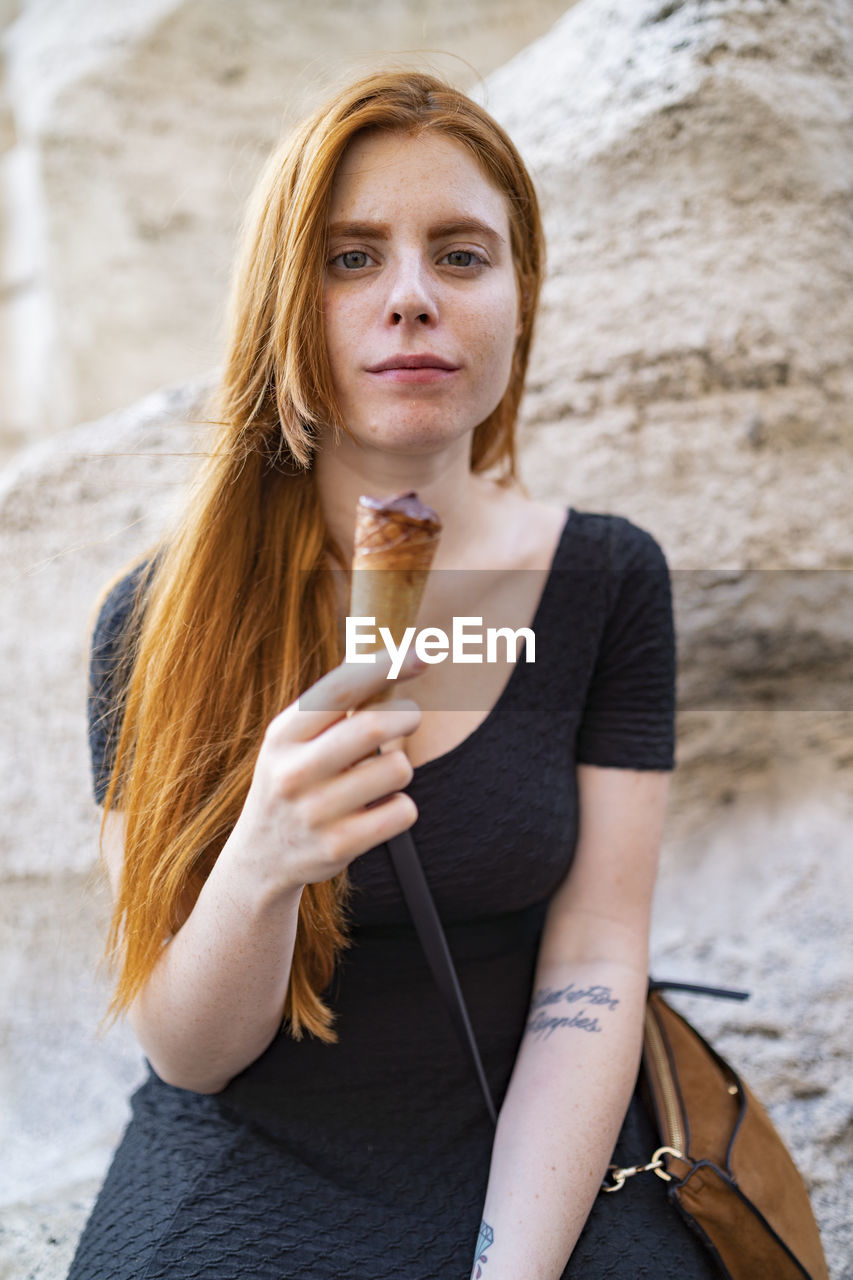 Redhead woman with half eaten ice cream cone looking at camera