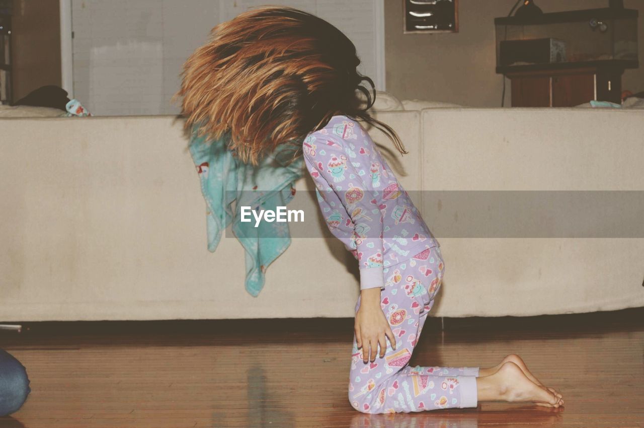 Side view of girl tossing hair while kneeling on hardwood floor at home