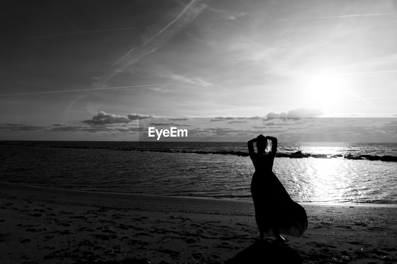 Silhouette woman standing at beach against sky during sunset