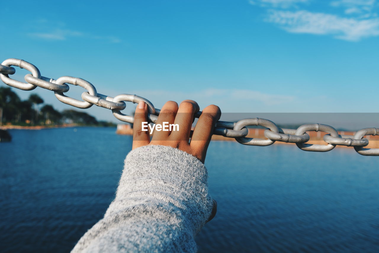 Close-up of hand against blue sea and sky