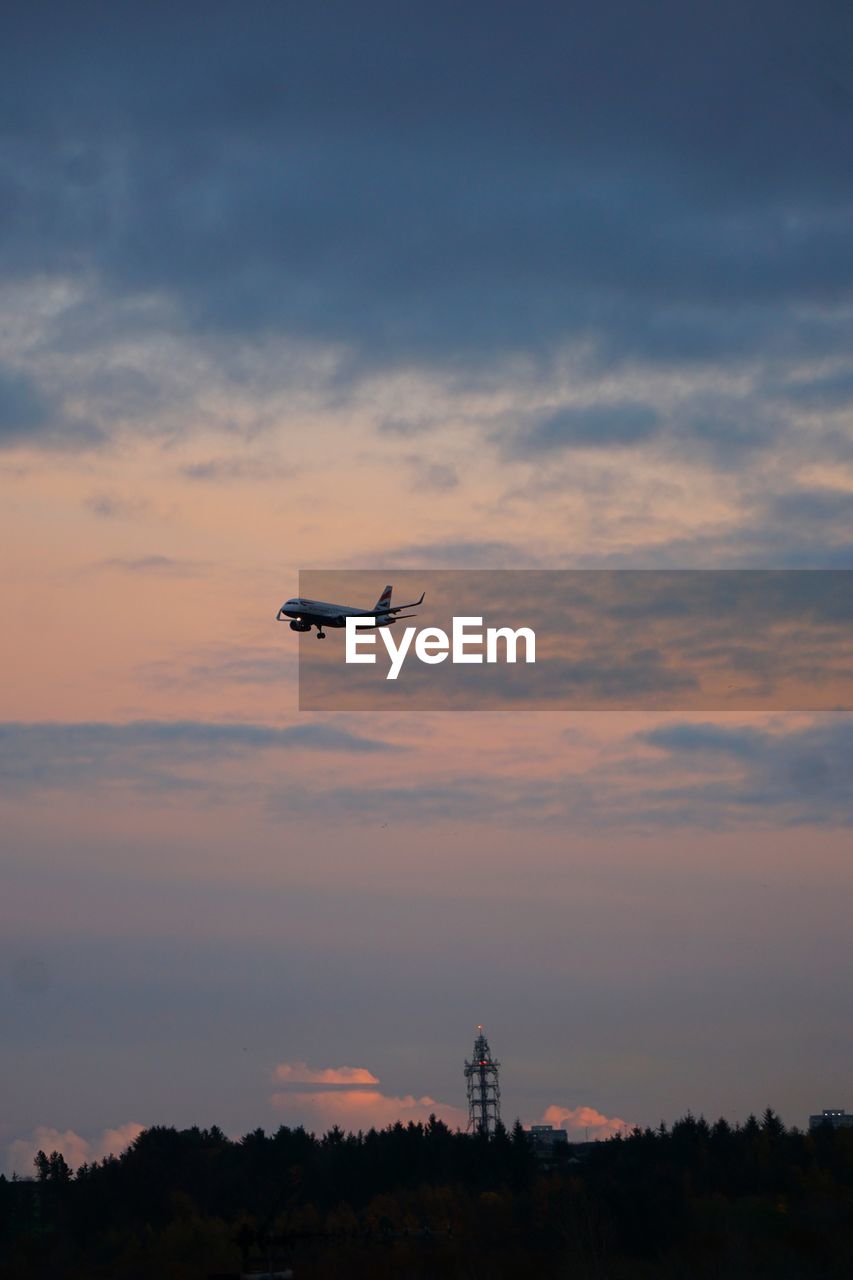 low angle view of airplane flying against cloudy sky during sunset