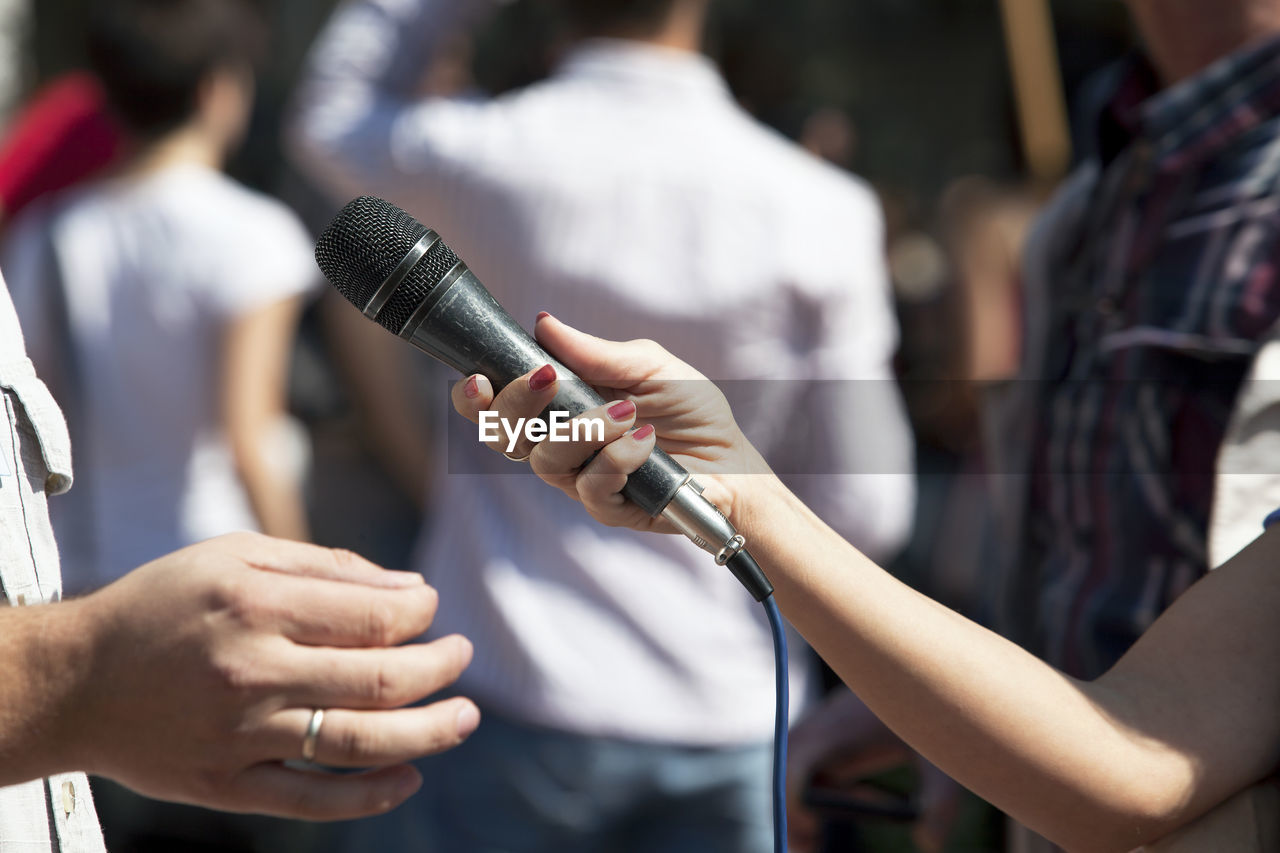 Cropped hand of journalist holding microphone for man