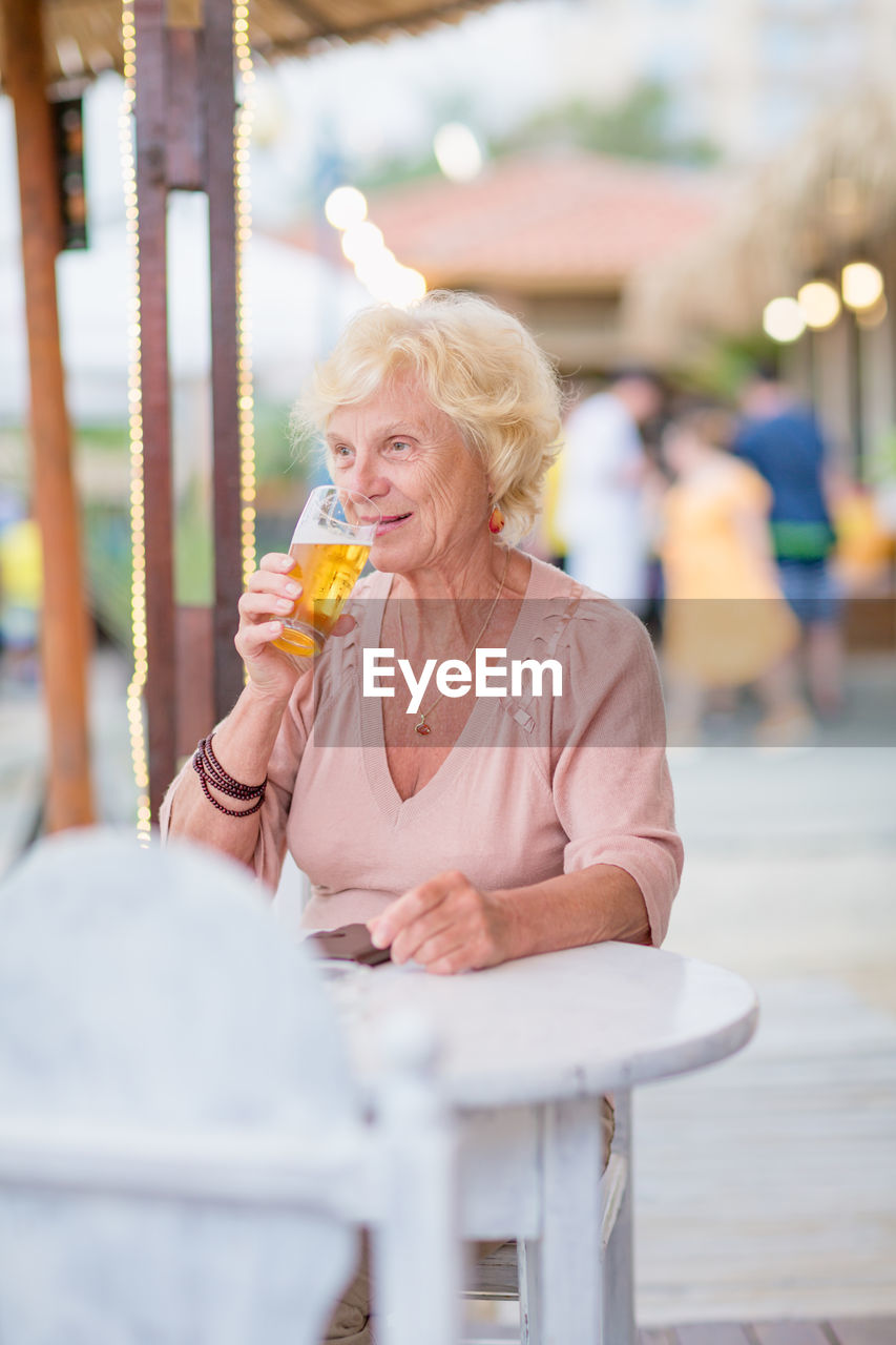 Mature woman sitting at a table in a summer cafe and drinking beer