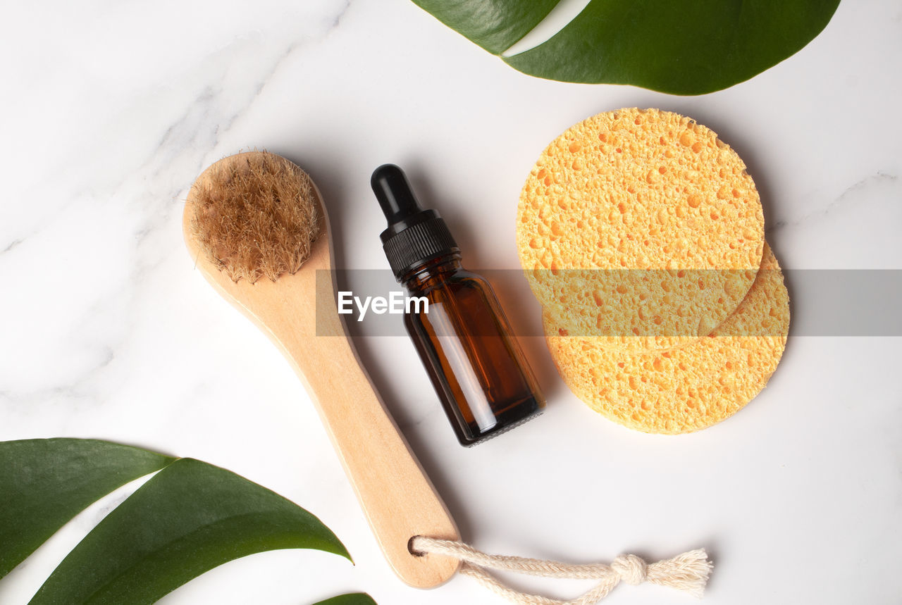 Cosmetic serum in brown glass bottle and body brush on a light beige background with monstera palm