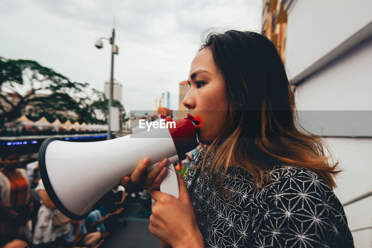 Woman holding megaphone while looking away against sky