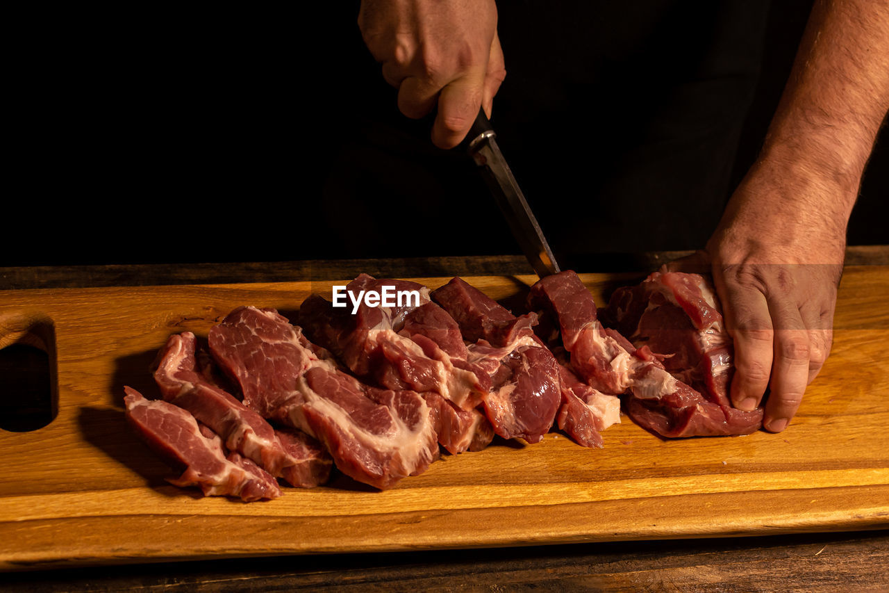 food and drink, food, meat, freshness, hand, red meat, raw food, one person, cutting board, beef, kitchen knife, cooking, preparing food, indoors, dish, cutting, wood, occupation, chopping, goat meat, cuisine, slice, table, kobe beef, pork, chef, close-up, men, steak