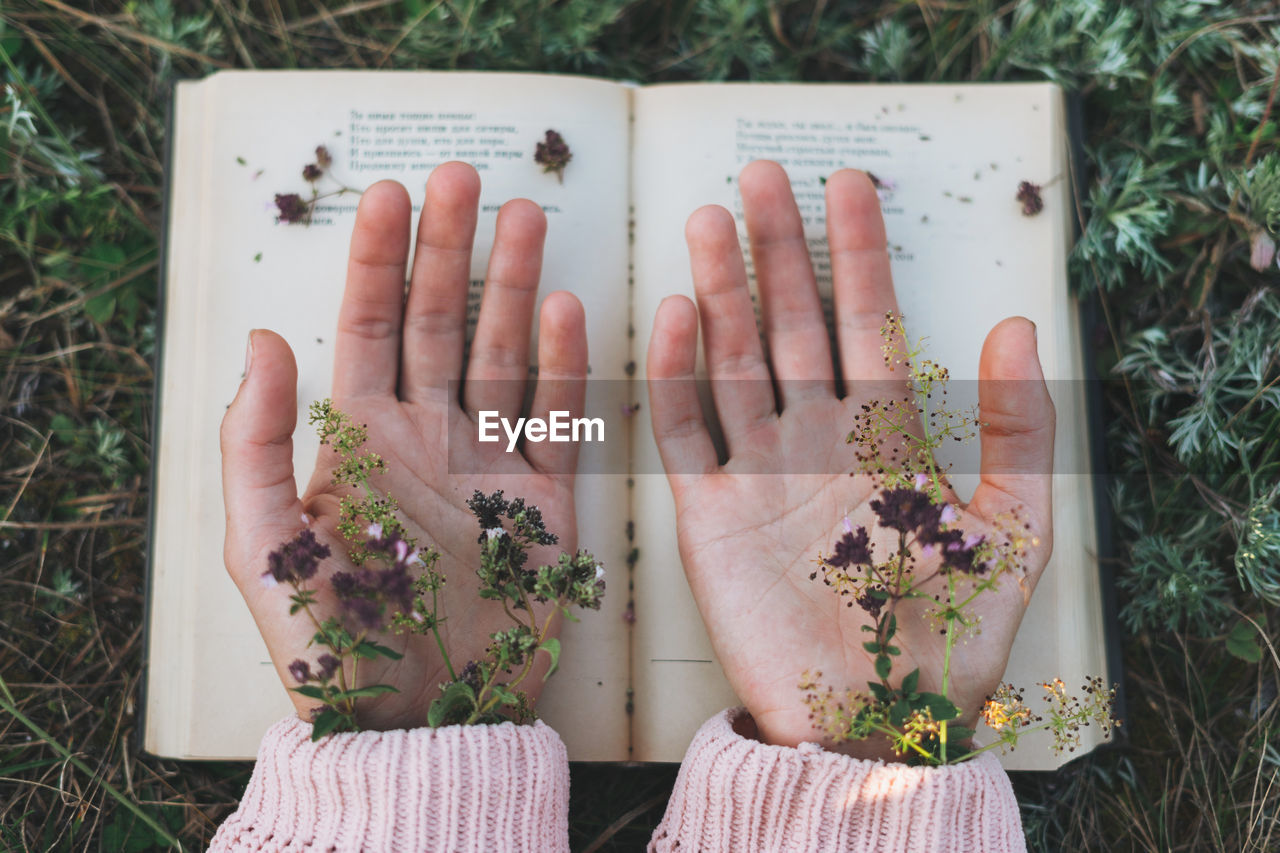 Directly above shot of woman hand with flower and book outdoors