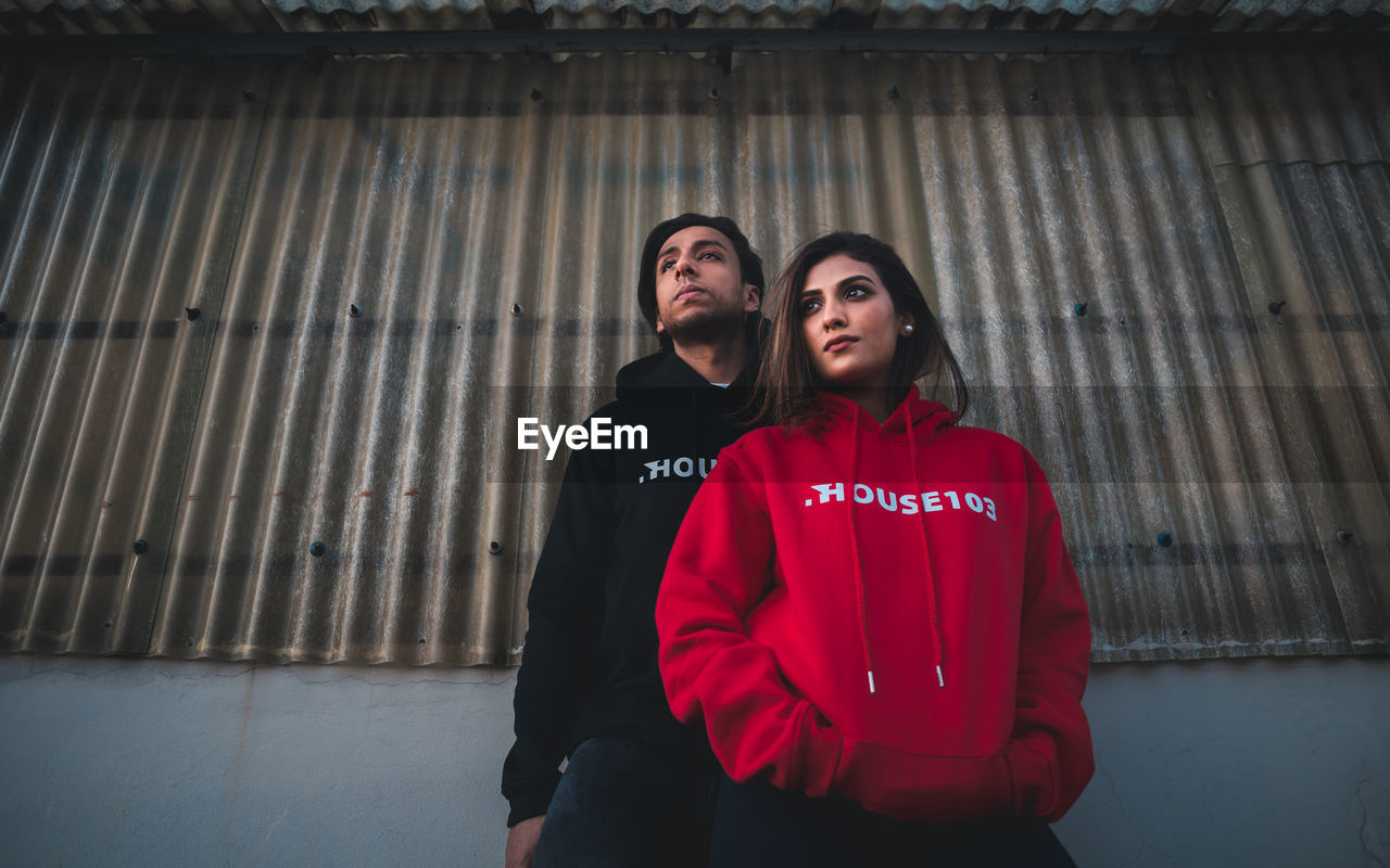 Young couple looking away while standing against corrugated wall