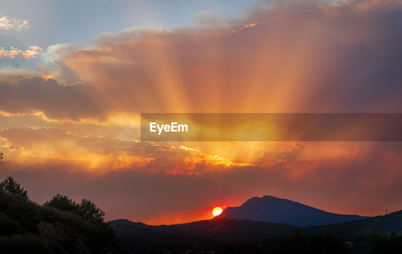 mountain, sky, environment, beauty in nature, cloud, landscape, sunrise, scenics - nature, dawn, nature, afterglow, land, dramatic sky, sun, no people, mountain range, morning, tree, orange color, red sky at morning, outdoors, travel destinations, red, silhouette, mountain peak, travel, forest, tranquility, horizon, sunlight, plant, sunbeam, non-urban scene, multi colored, tourism, tranquil scene, idyllic, fog, cloudscape