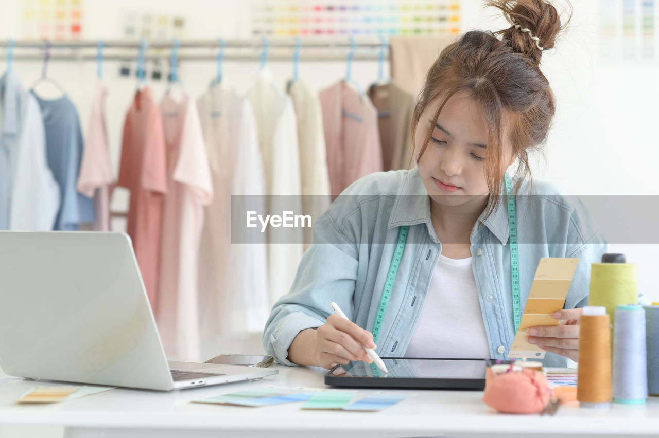 A young woman tailors in a designer's workspace with design equipment.
